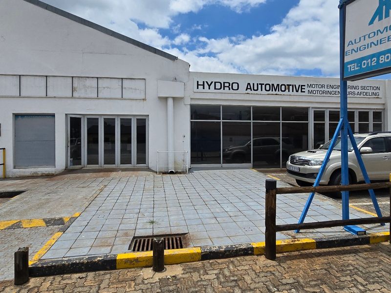 Front elevation of an industrial automotive engineering facility featuring a paved forecourt, large glass storefront, and roller shutter access.