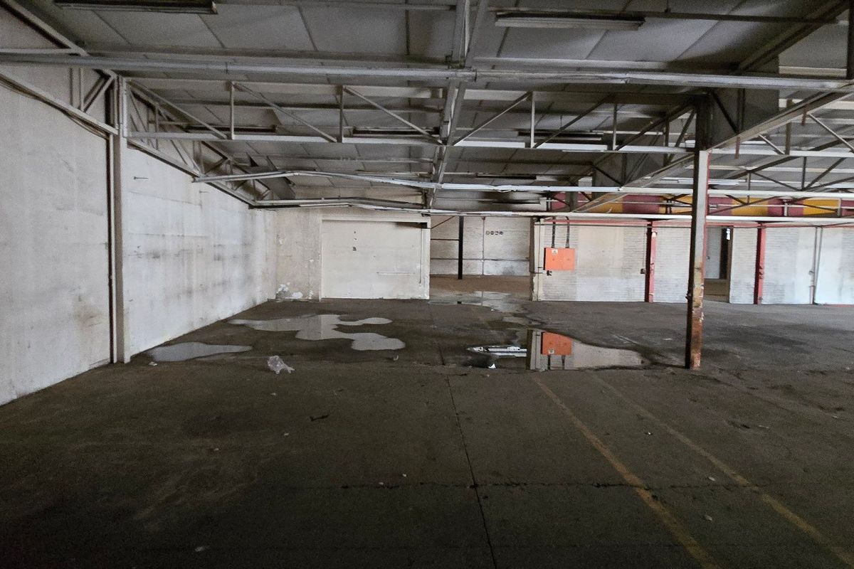 Large open-plan industrial warehouse space featuring exposed steel roof trusses, concrete flooring, and functional utility infrastructure.