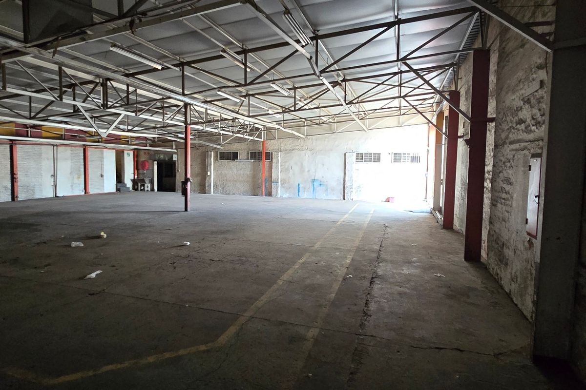 Spacious industrial warehouse area featuring exposed steel roof trusses, concrete flooring, and steel support columns, suitable for storage or manufacturing operations.