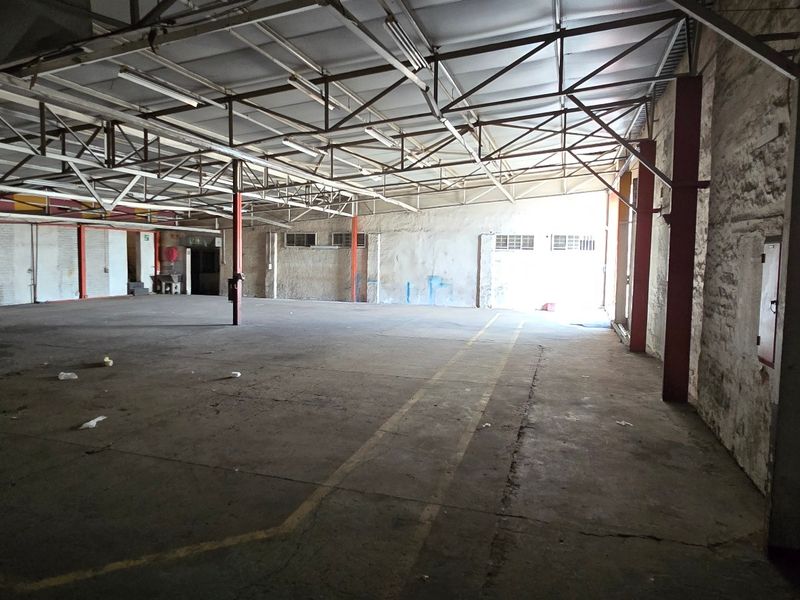 Spacious industrial warehouse area featuring exposed steel roof trusses, concrete flooring, and steel support columns, suitable for storage or manufacturing operations.