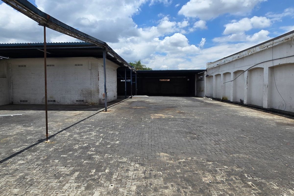 Spacious industrial yard area featuring paved ground, covered loading bays, and robust brick masonry walls, suitable for logistics or storage operations.
