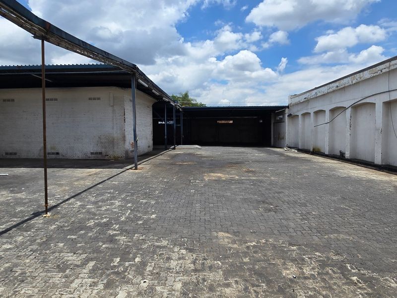 Spacious industrial yard area featuring paved ground, covered loading bays, and robust brick masonry walls, suitable for logistics or storage operations.