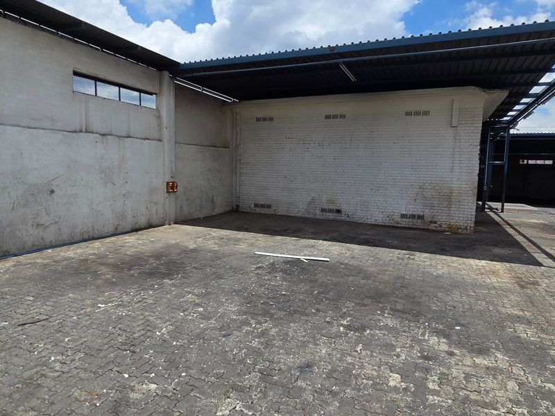 Industrial rear yard area featuring a paved surface, covered loading bay, and secure perimeter walls suitable for logistics or storage operations.