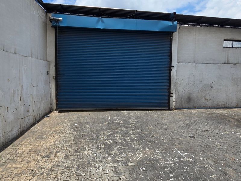 Industrial yard area featuring a large blue roller shutter door, high perimeter walls, and paved ground surface, suitable for loading and logistics access.