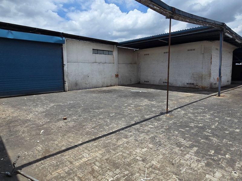 Industrial rear yard featuring a large roller shutter door, paved surface, and covered loading area with steel structural supports.