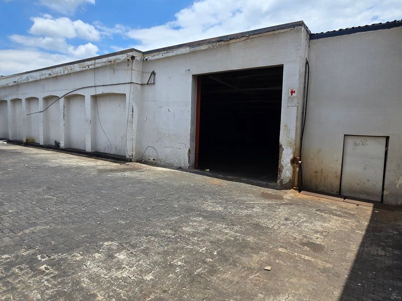 Rear industrial yard area featuring paved surfacing, masonry walls, and a large roller shutter access point for loading or storage.