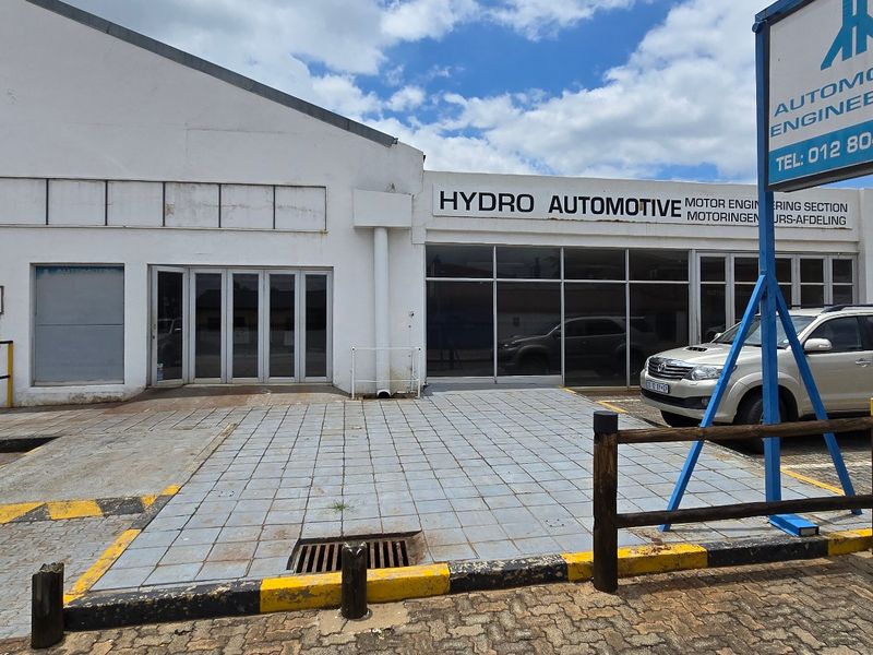 Front elevation of an industrial property featuring a roller shutter door, glass storefront, and paved forecourt with prominent business signage.