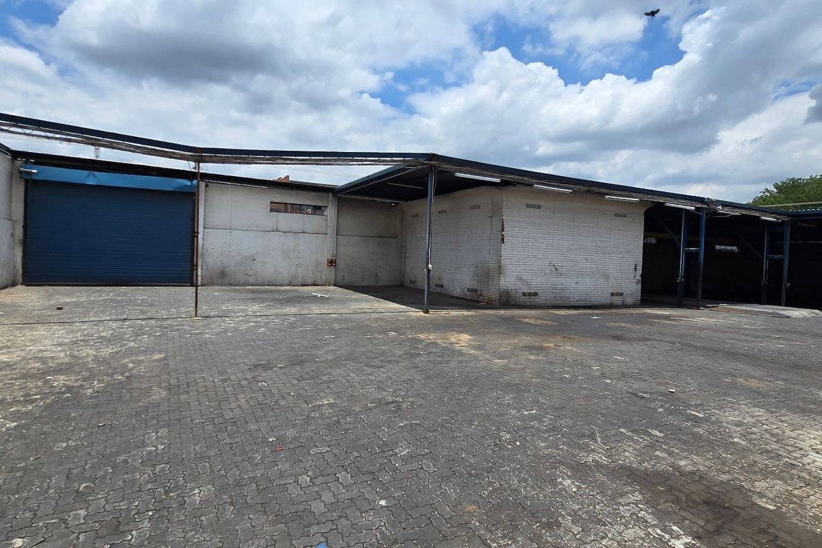 Spacious industrial yard featuring a large paved area, covered loading bay, and a secure roller shutter door access point.