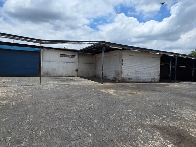 Spacious industrial yard featuring a large paved area, covered loading bay, and a secure roller shutter door access point.