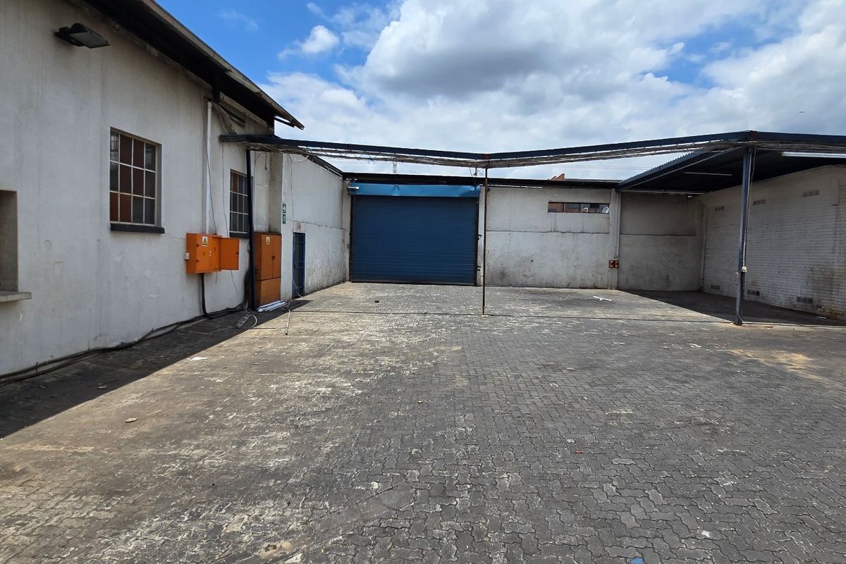 Industrial rear yard featuring a paved surface, covered loading area, and a large roller shutter door for efficient access.