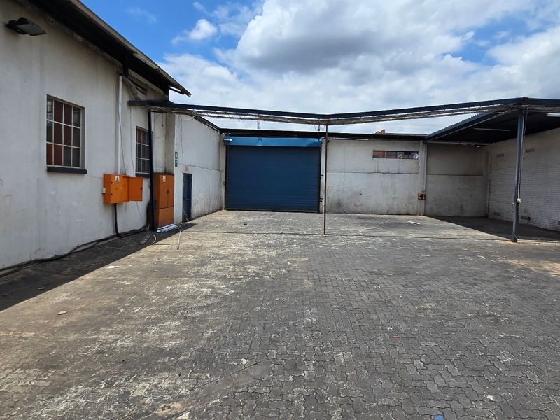 Industrial rear yard featuring a paved surface, covered loading area, and a large roller shutter door for efficient access.