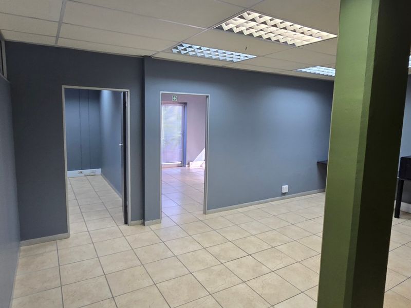 An open-plan commercial office space featuring neutral grey walls, ceramic tiled flooring, and a suspended ceiling with recessed lighting.
