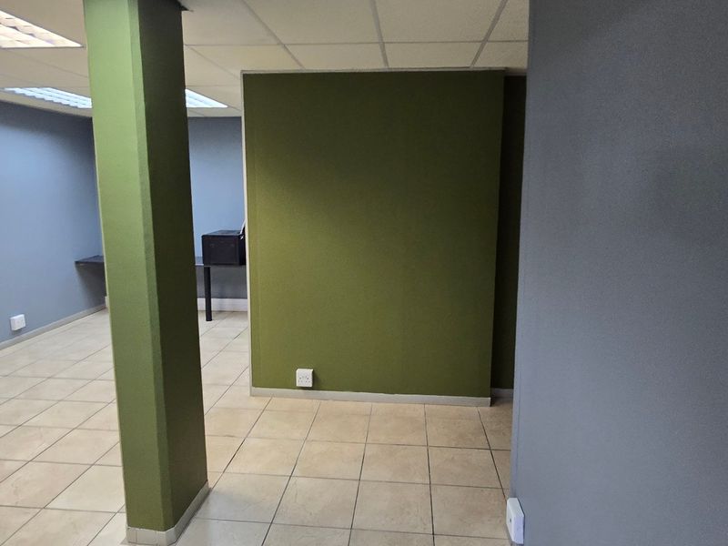 An empty commercial office space featuring ceramic floor tiles, a structural column, and a suspended ceiling with recessed lighting.