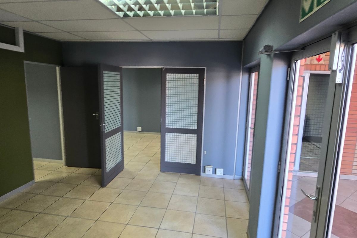 A vacant commercial office space featuring tiled flooring, a suspended ceiling with recessed lighting, and glass-panelled doors leading to an adjacent room.