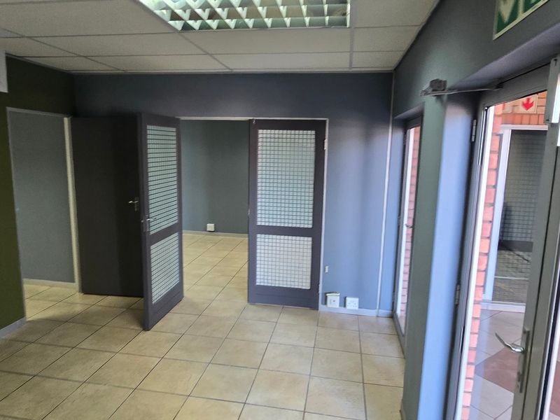 A vacant commercial office space featuring tiled flooring, a suspended ceiling with recessed lighting, and glass-panelled doors leading to an adjacent room.
