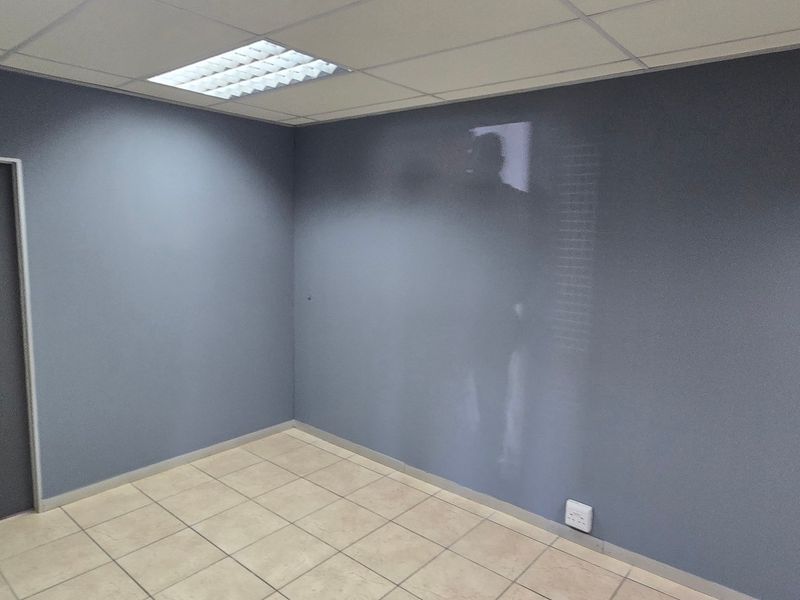 A vacant office space featuring neutral grey walls, tiled flooring, and a suspended ceiling with recessed lighting.