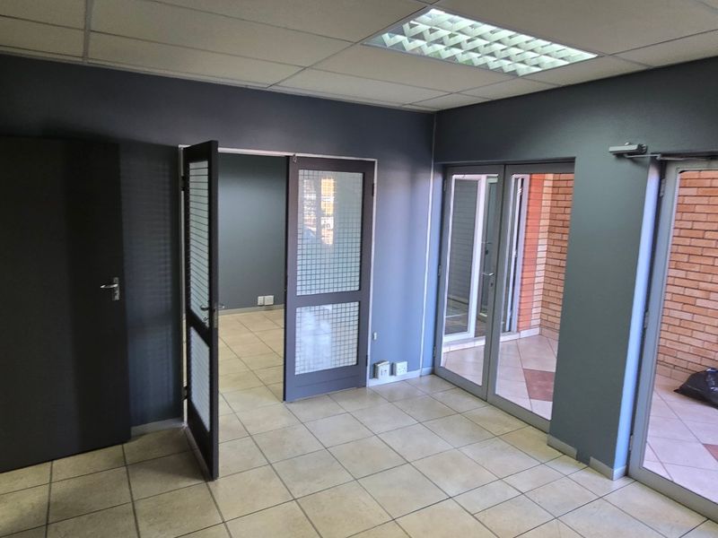 A vacant commercial office space featuring tiled flooring, suspended ceilings with recessed lighting, and multiple glass-panelled doors leading to an exterior walkway.