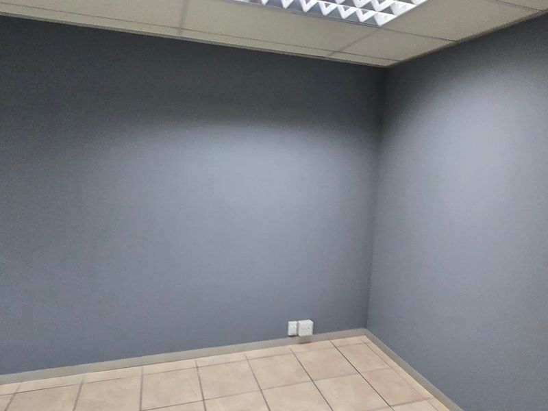 A clean, empty office space featuring grey painted walls, tiled flooring, and recessed ceiling lighting, suitable for a professional workspace.