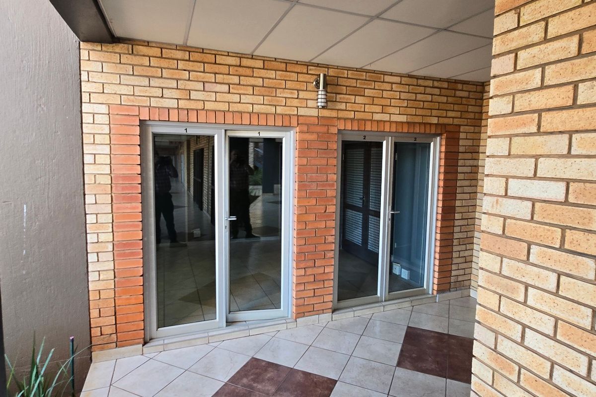A covered outdoor patio area featuring exposed brick walls, tiled flooring, and multiple sliding glass door entrances to the commercial interior space.