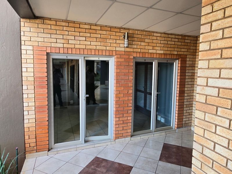 A covered outdoor patio area featuring exposed brick walls, tiled flooring, and multiple sliding glass door entrances to the commercial interior space.