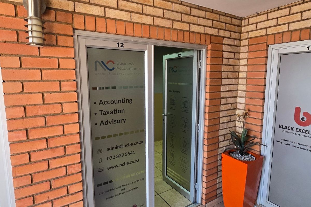 Commercial office entrance featuring exposed brickwork, aluminium framed glass doors, and clear business signage for units 12 and 13.