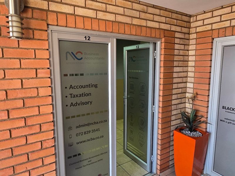 Commercial office entrance featuring exposed brickwork, aluminium framed glass doors, and clear business signage for units 12 and 13.