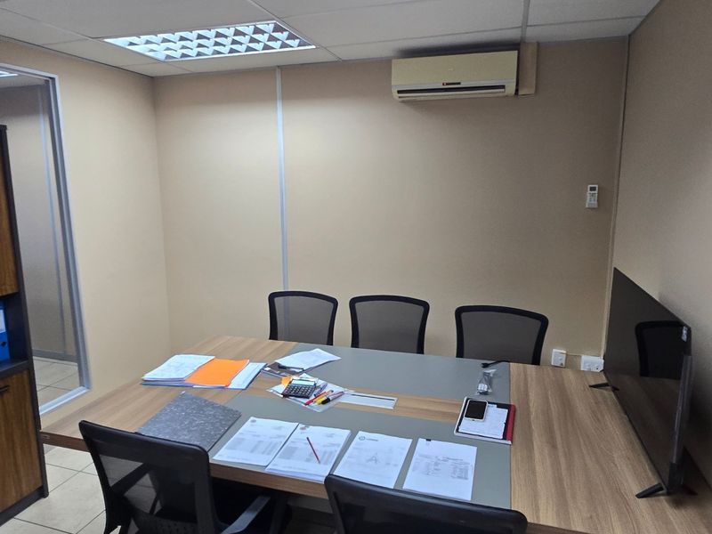 A functional commercial office space featuring a suspended ceiling, recessed lighting, wall-mounted air conditioning, and built-in storage cabinetry.