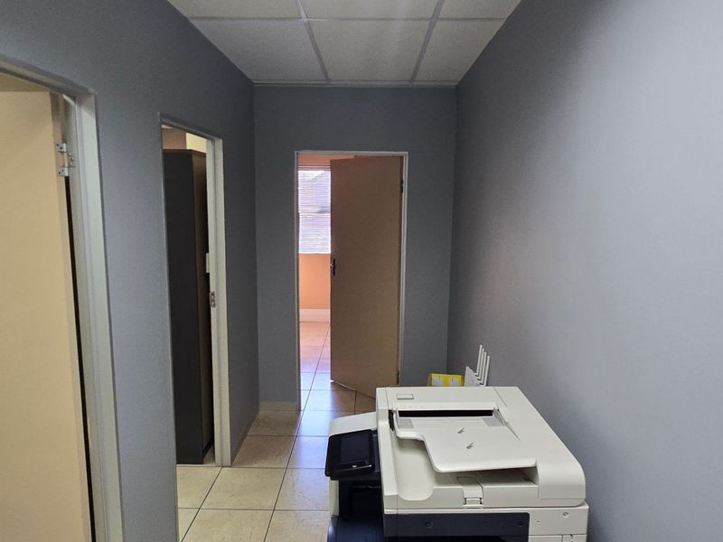 A functional commercial hallway featuring tiled flooring, a suspended ceiling, and multiple internal access doors connecting to adjacent office spaces.
