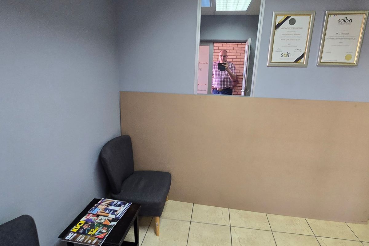 A small office space featuring tiled flooring and a partition wall, currently used as a waiting or reception area.