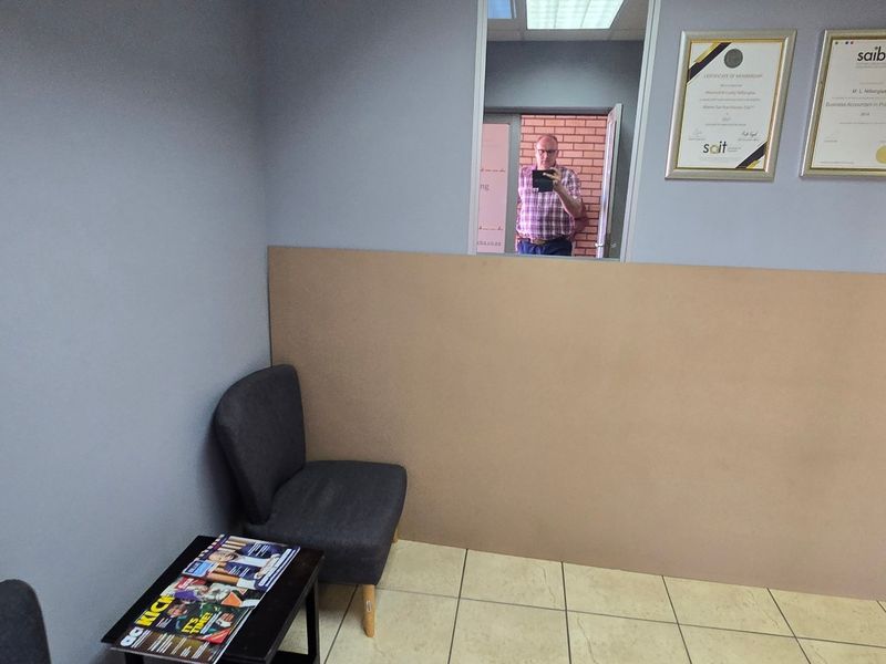 A small office space featuring tiled flooring and a partition wall, currently used as a waiting or reception area.