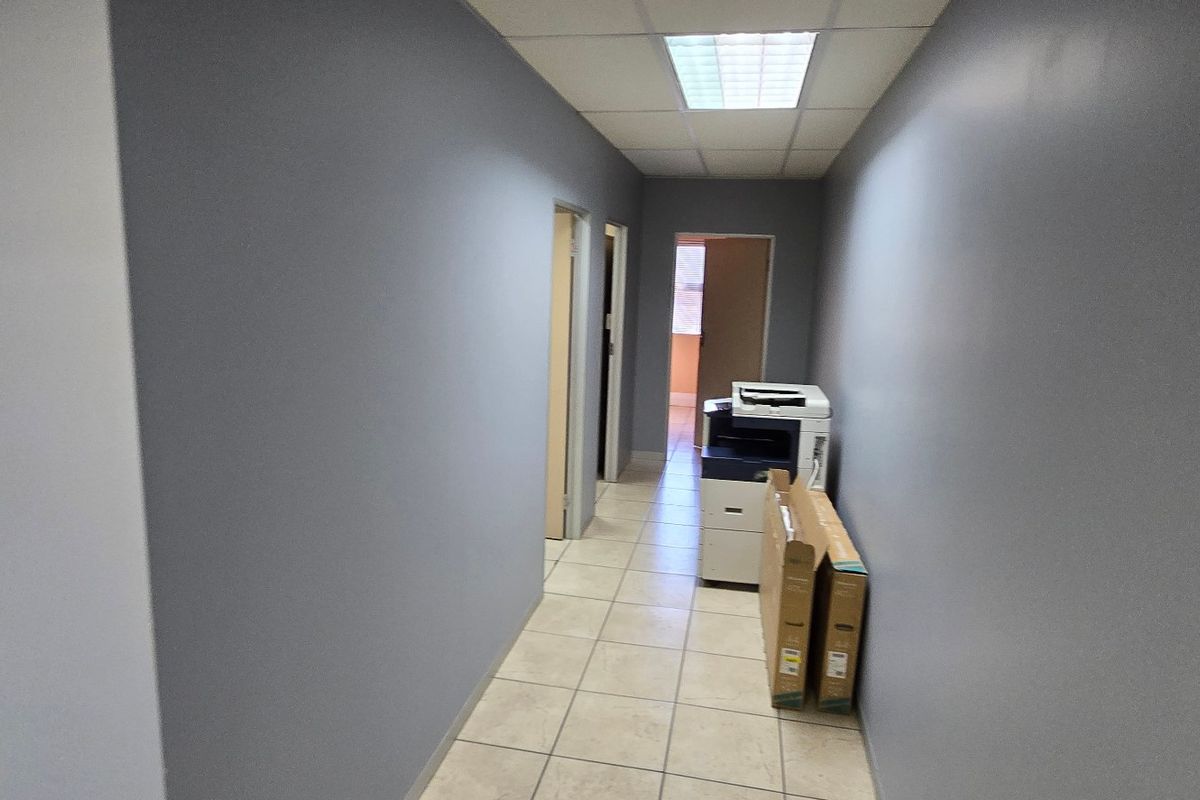 A clean, functional commercial hallway featuring tiled flooring, a suspended ceiling with recessed lighting, and access to multiple internal office spaces.