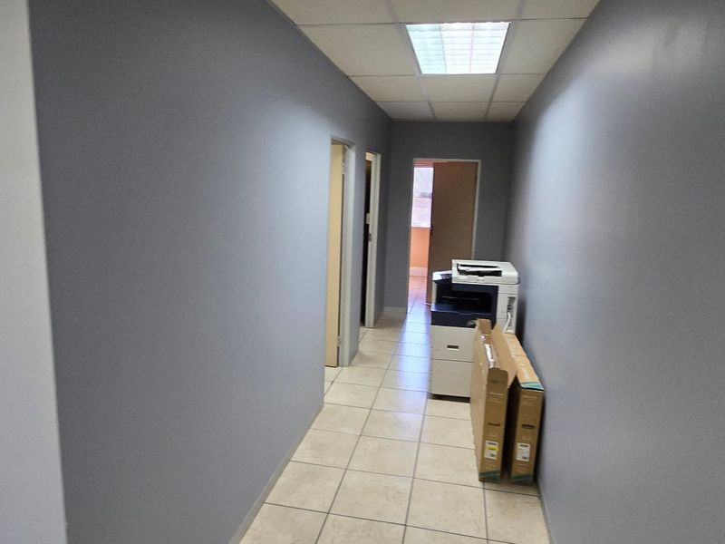A clean, functional commercial hallway featuring tiled flooring, a suspended ceiling with recessed lighting, and access to multiple internal office spaces.