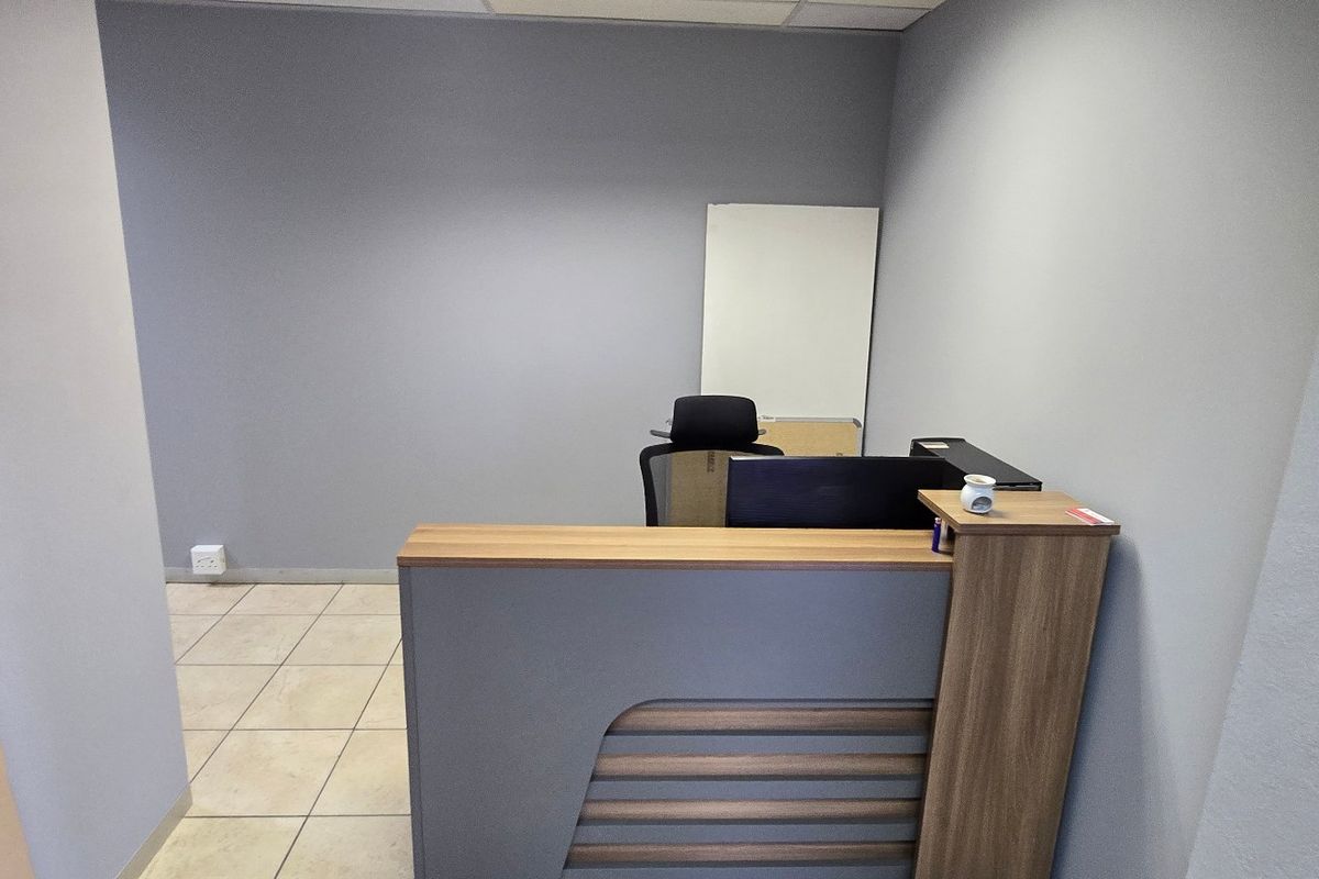 A functional office space featuring a modern built-in reception desk, neutral grey walls, and durable tiled flooring.