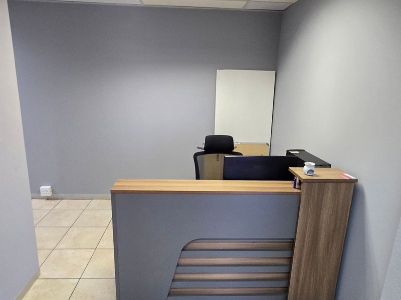 A functional office space featuring a modern built-in reception desk, neutral grey walls, and durable tiled flooring.