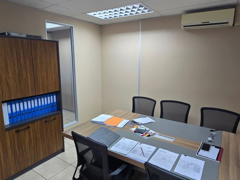 A functional commercial office space featuring tiled flooring, built-in storage cabinetry, recessed ceiling lighting, and a wall-mounted air conditioning unit.