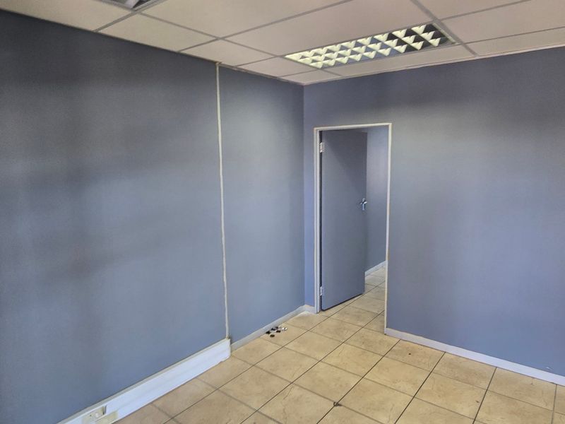 An empty commercial office space featuring ceramic tiled flooring, a suspended ceiling with recessed lighting, and a glass partition wall.