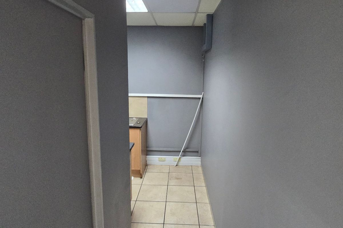A small, empty commercial kitchen area featuring tiled flooring, drop ceiling, and basic built-in cabinetry with a sink.
