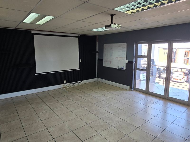 Spacious commercial office featuring tiled flooring, suspended ceiling with recessed lighting, built-in projector, and large aluminium sliding doors providing natural light.