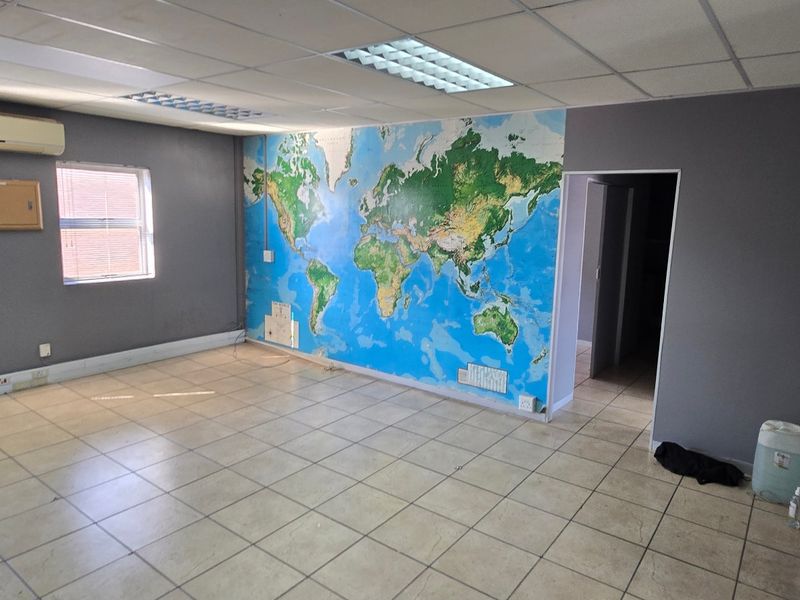 An empty commercial office space featuring ceramic tiled flooring, a suspended ceiling with recessed lighting, and a wall-mounted air conditioning unit.
