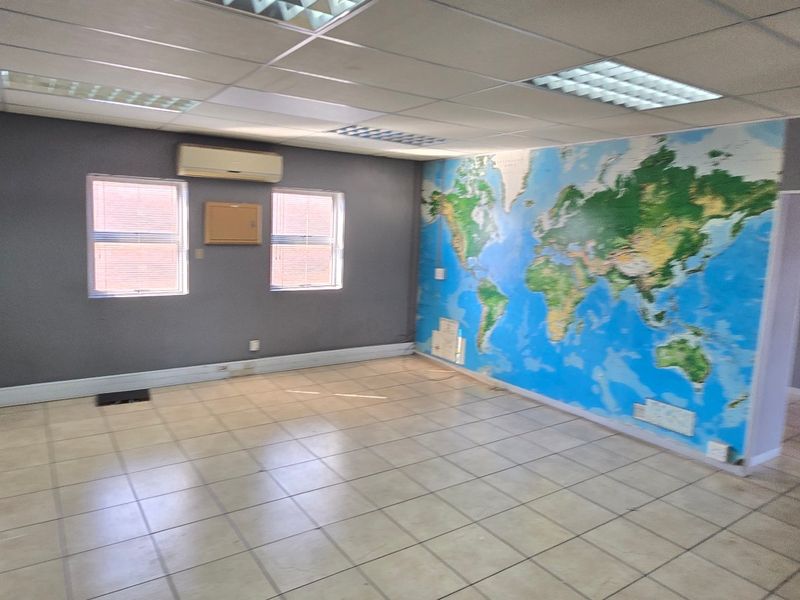 An empty commercial office space featuring ceramic tiled flooring, a suspended ceiling with recessed lighting, and a wall-mounted air conditioning unit.