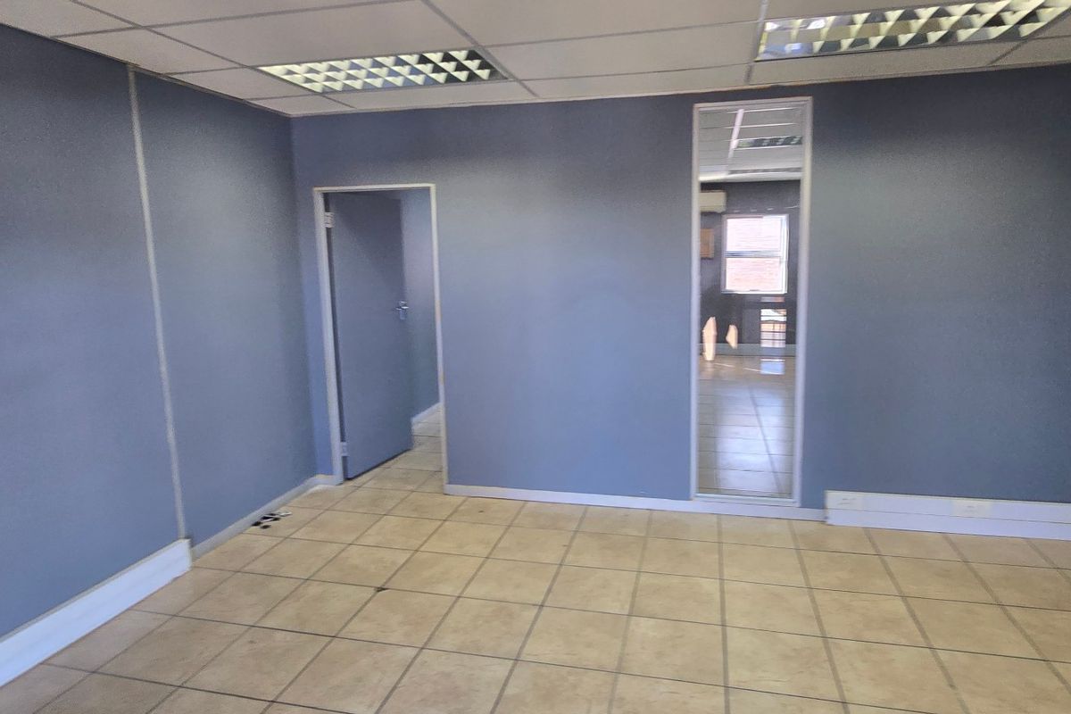 A vacant commercial office space featuring neutral ceramic floor tiles, a suspended ceiling with recessed lighting, and blue painted walls.