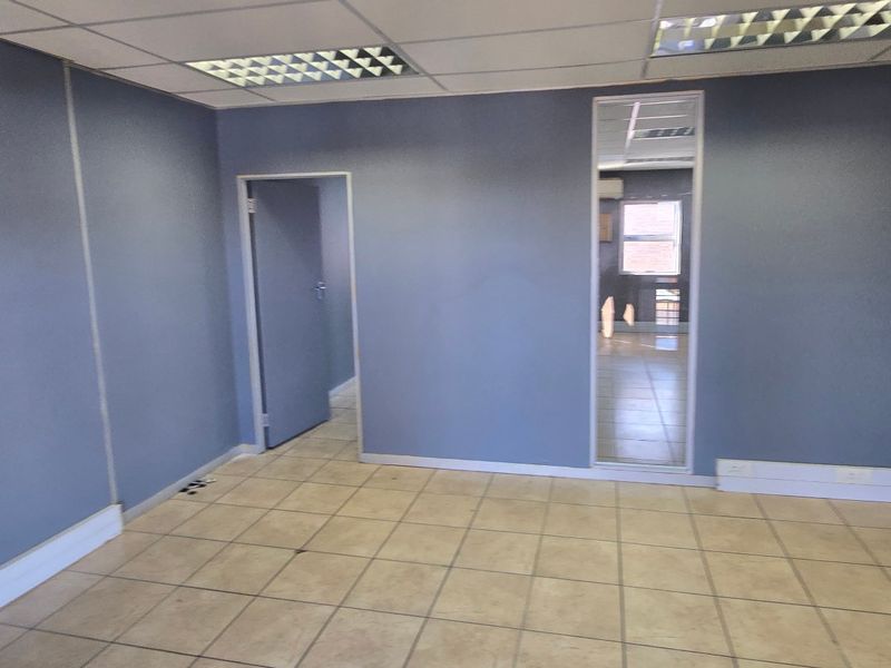 A vacant commercial office space featuring neutral ceramic floor tiles, a suspended ceiling with recessed lighting, and blue painted walls.