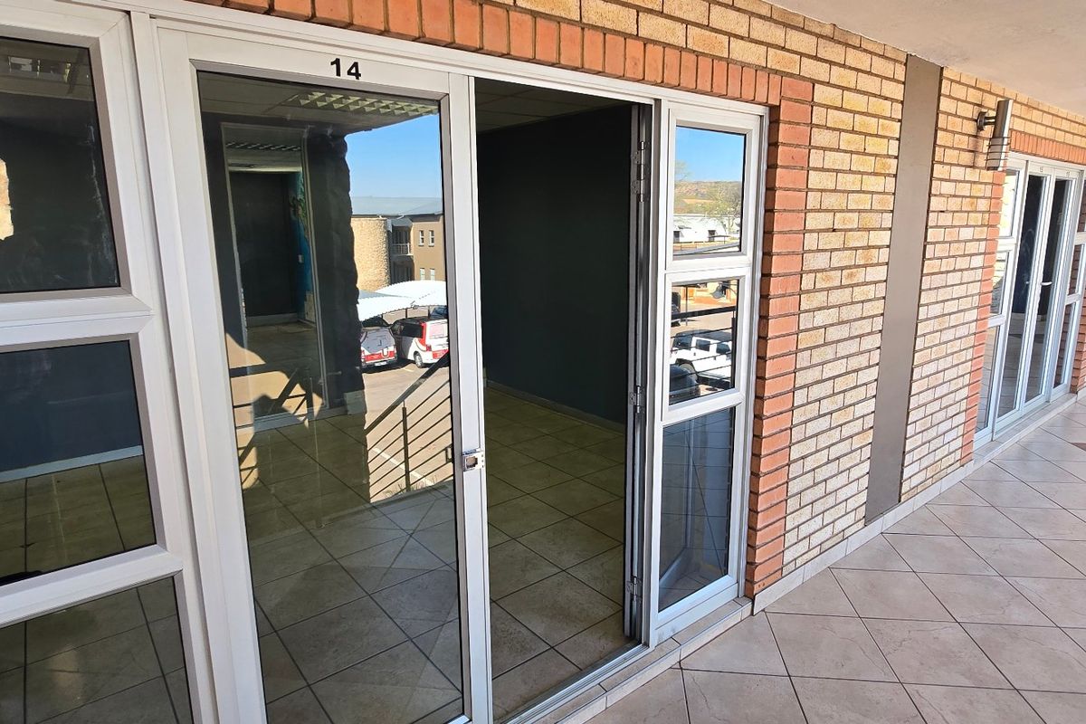 Exterior view of a commercial unit entrance featuring a brick facade, tiled walkway, and aluminium sliding glass doors.