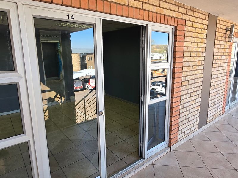 Exterior view of a commercial unit entrance featuring a brick facade, tiled walkway, and aluminium sliding glass doors.