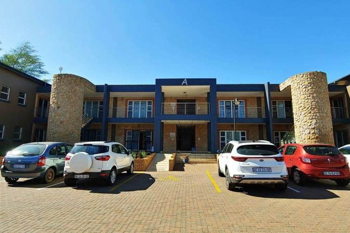 Front elevation of a commercial office building featuring stone-clad pillars, a paved parking area, and a two-story facade with balcony access.