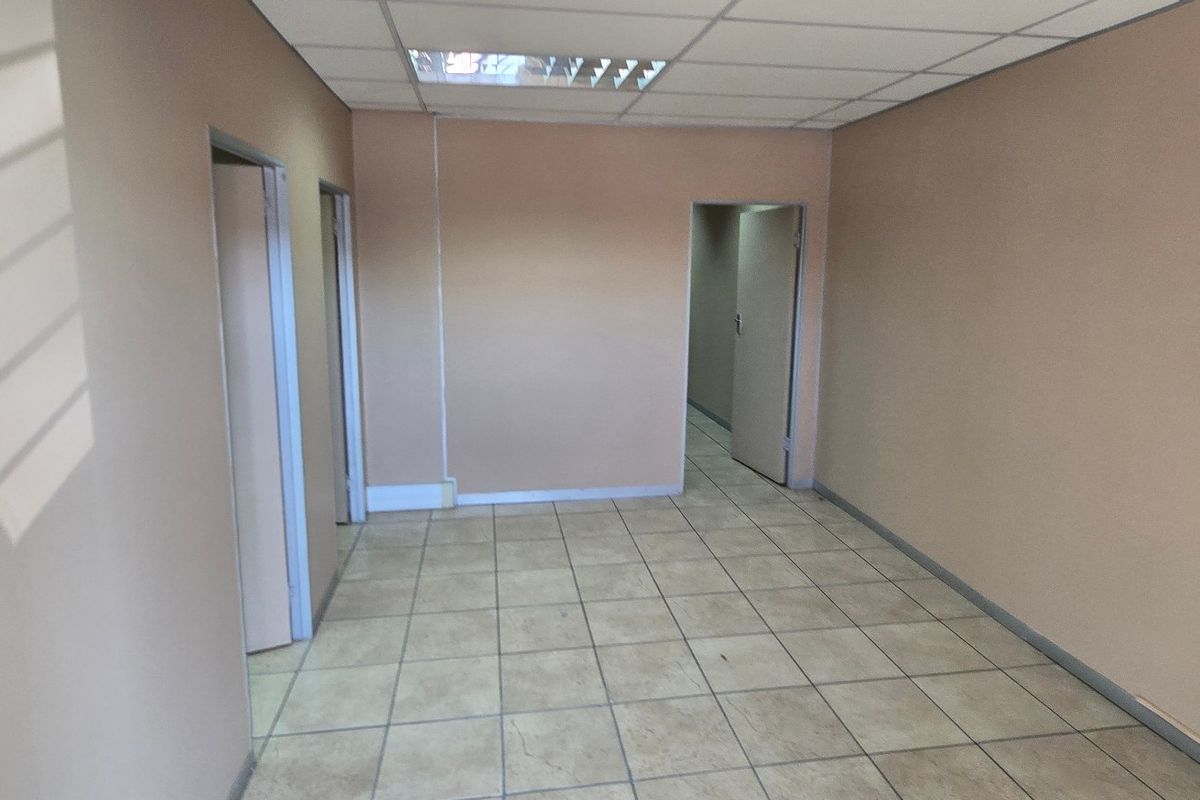 An empty commercial office space featuring neutral walls, tiled flooring, and a suspended ceiling with recessed lighting.