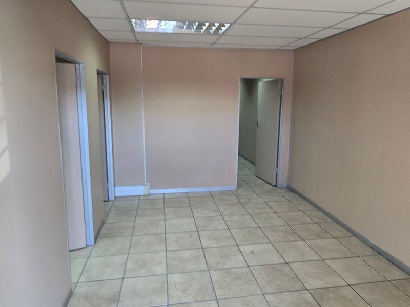 An empty commercial office space featuring neutral walls, tiled flooring, and a suspended ceiling with recessed lighting.