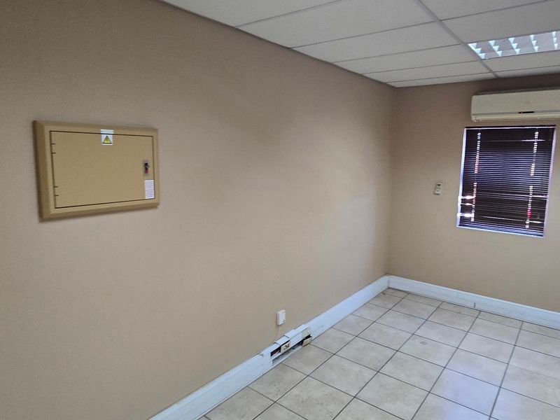 A vacant commercial office space featuring ceramic tiled flooring, a suspended ceiling with recessed lighting, and a wall-mounted air conditioning unit.