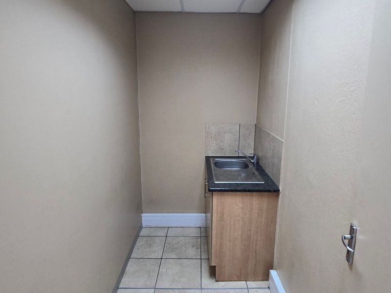 A compact utility or scullery area featuring a built-in sink, laminate cabinetry, and tiled flooring, providing functional space for basic preparation or wash-up tasks.