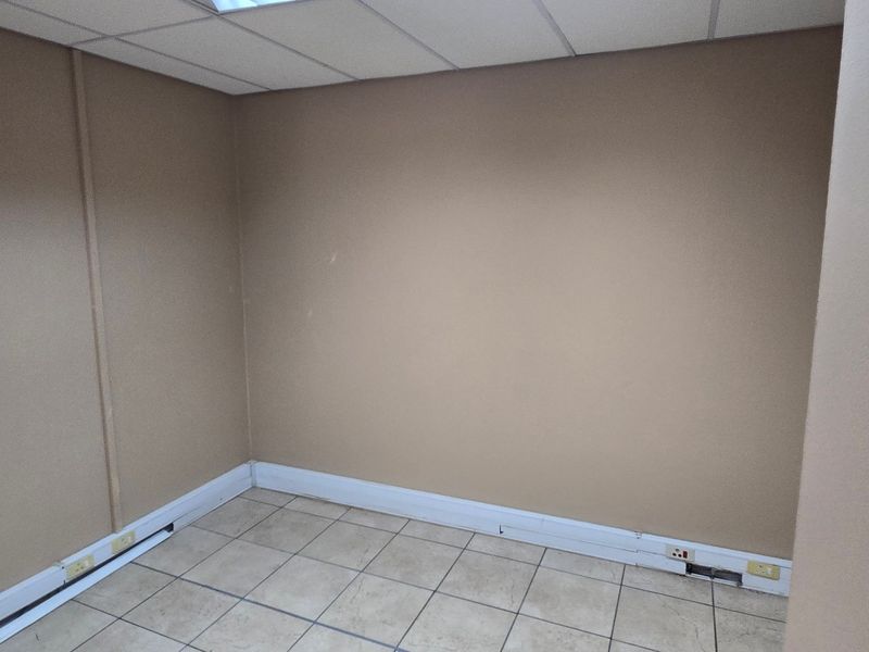 A vacant office space featuring neutral wall tones, ceramic tiled flooring, and a suspended ceiling, suitable for a professional workspace.